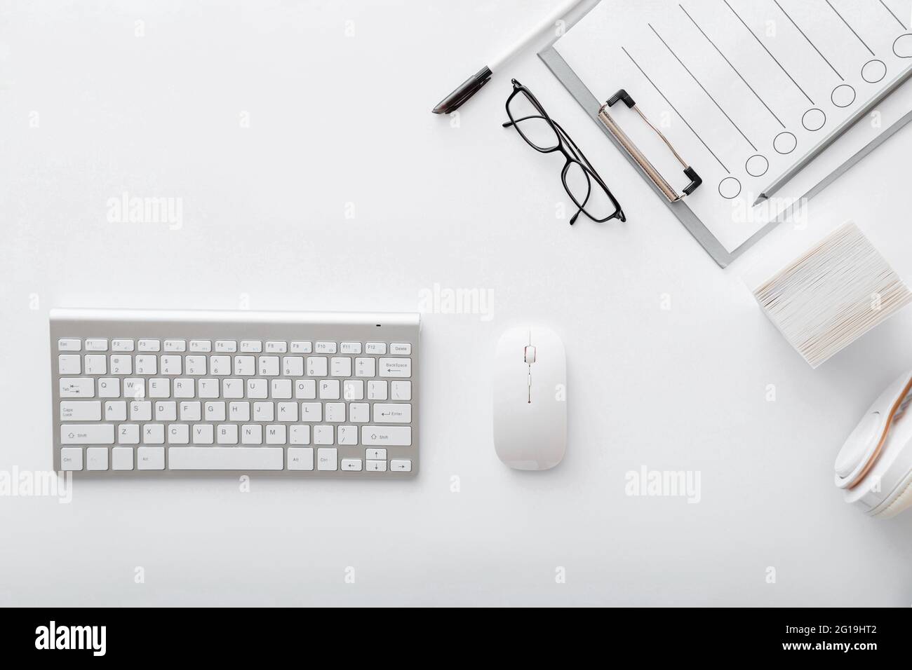Arbeitsplatz mit Tastatur Maus Brille Papiere. Flaches Lay White Schreibtisch Büro Arbeitsplatz pc-Computer. Weiße silberne Tischtastatur, Ansicht von oben mit Kopierplatz Stockfoto