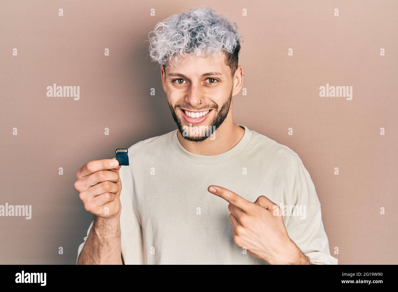 Junger hispanischer Mann mit modernen gefärbten Haaren, die sdxc-Karte halten, lächelt glücklich und zeigt mit Hand und Finger Stockfoto