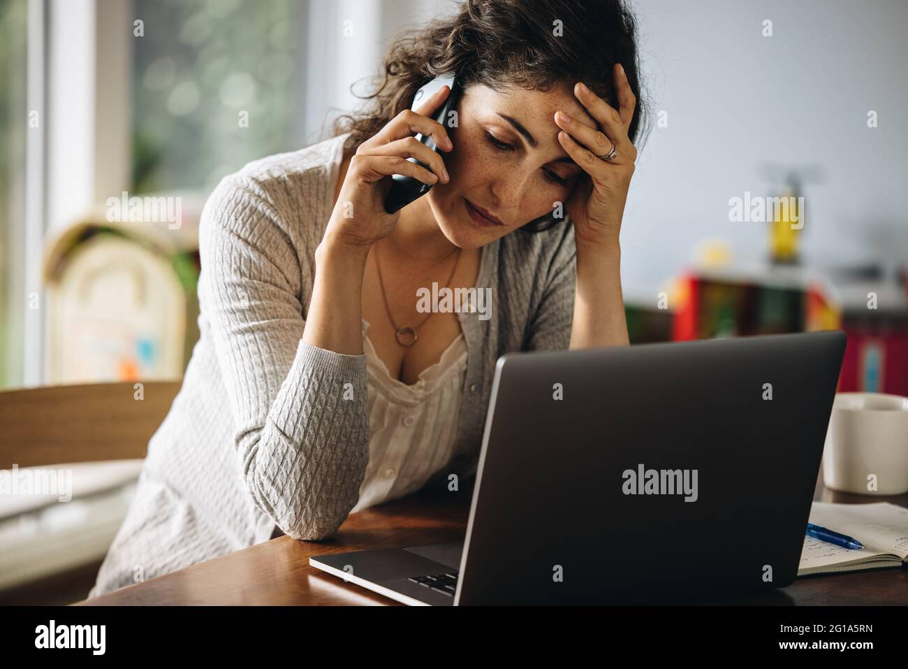 Frau, die ihren Kopf hält und mit dem Mobiltelefon spricht. Gestresste Frau, die von zu Hause aus telefoniert. Stockfoto