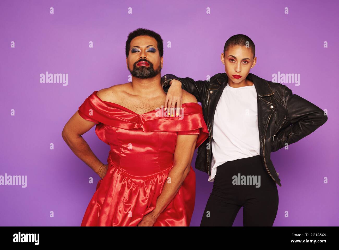 Androgyne männliche und weibliche posieren im Studio. Geschlecht queerer Mann im weiblichen Kleid mit Frau in männlicher Kleidung auf purpurem Hintergrund. Stockfoto
