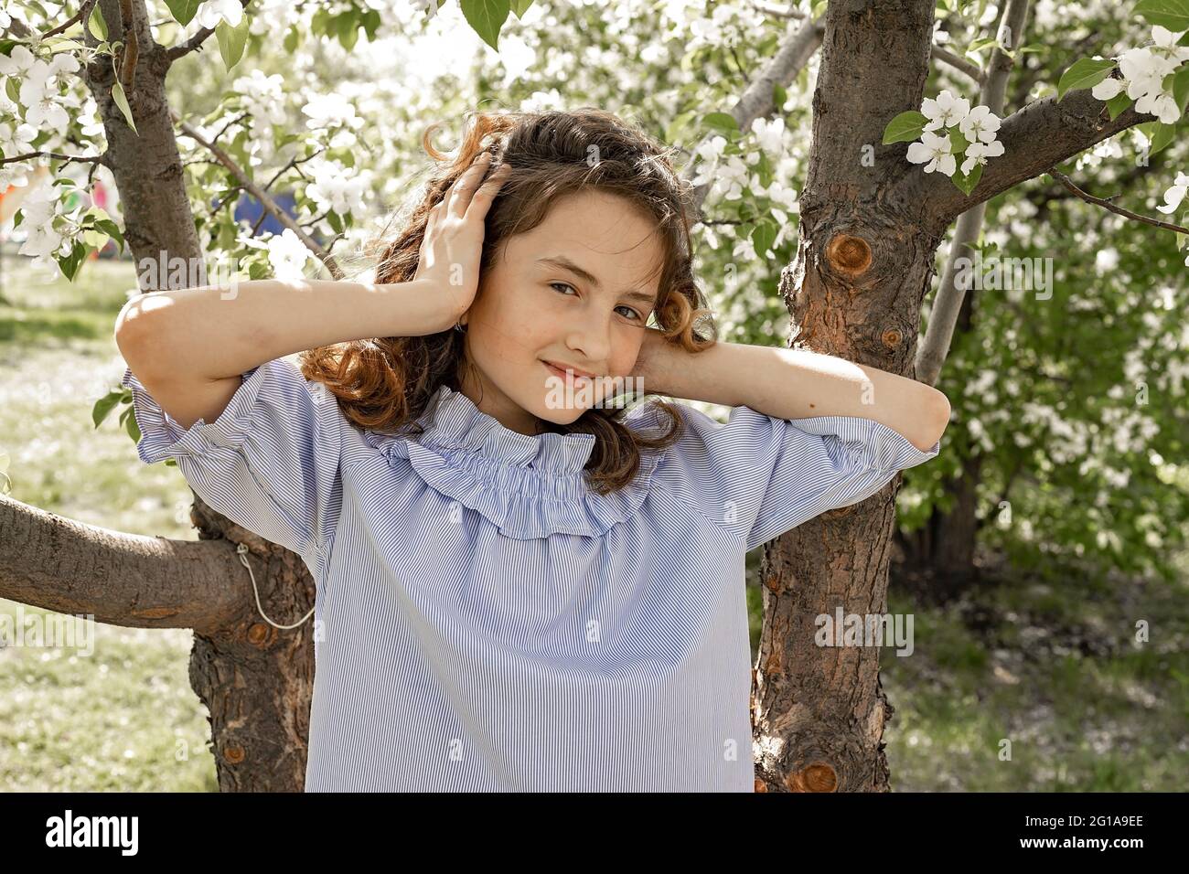 Lifestyle-Foto von einem glücklichen Kind. Nettes hübsches lächelndes Brünette Mädchen in einem blühenden Garten. Das Mädchen richtet ihre flatternden Haare im Wind und im Klo auf Stockfoto