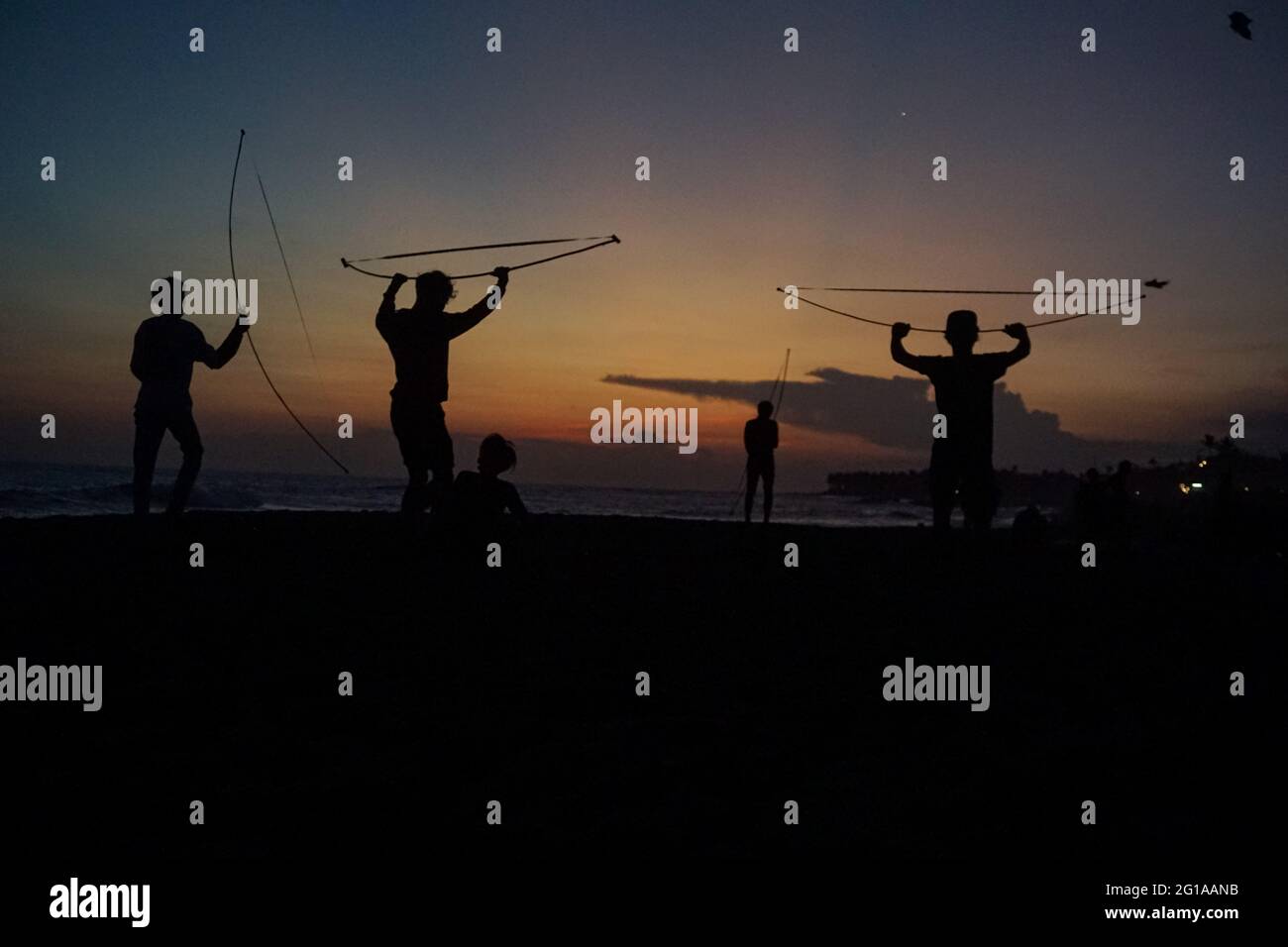 Badung, Bali, Indonesien. Juni 2021. Die Silhouette zeigt balinesische Jugendliche, die den Guangan-Sound testen. Guangan ist Teil des traditionellen Drachen aus Bambus und speziellen Band, die einen einzigartigen Klang machen kann, während der Wind weht. Die Kitesaison findet jedes Jahr zwischen Mai und September während der Trockenzeit statt und ist die beste Zeit für einen Besuch im Tourismus auf Bali. Die Farben des roten, weißen, schwarzen und gelblichen Goldes stellen die Inkarnation der balinesischen Hindu-Gottheiten dar. (Bild: © Dicky BisinglasiZUMA Wire) Stockfoto