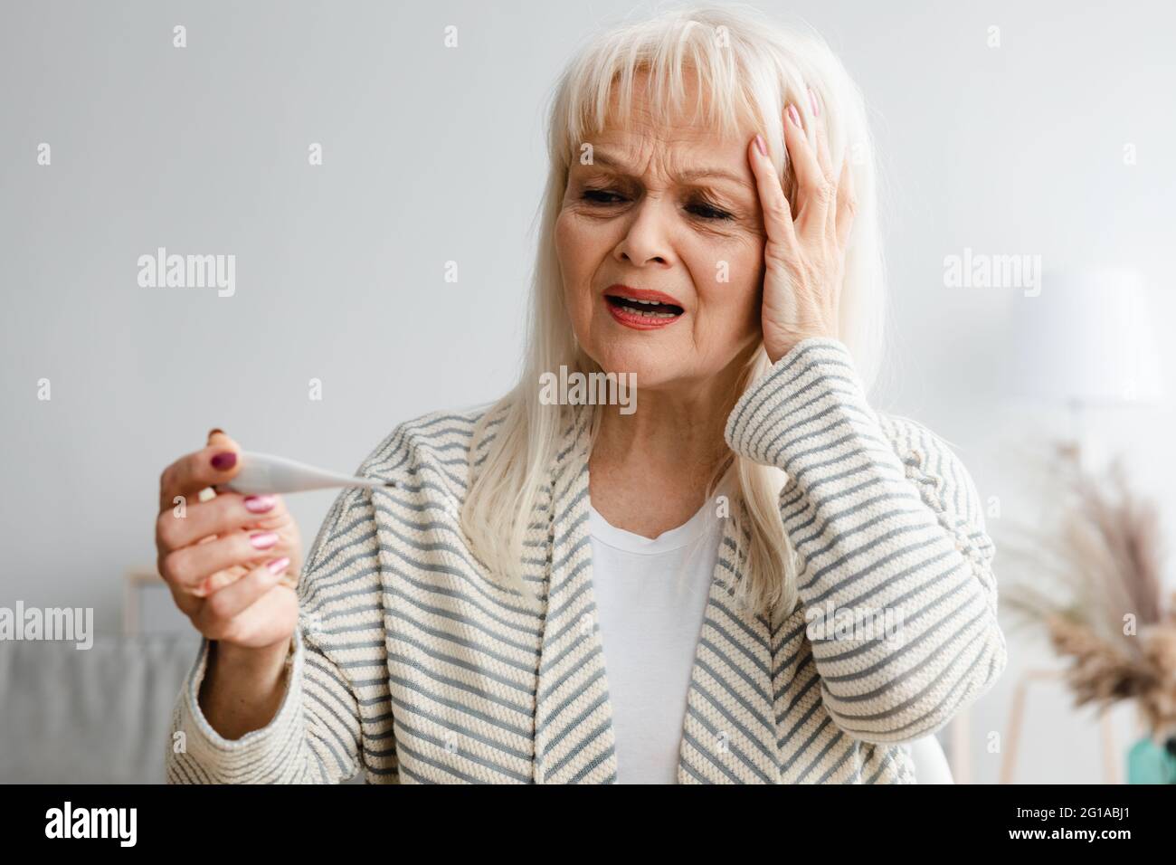 Erschrocken reife Dame Überprüfung Körpertemperatur Blick auf Thermometer Stockfoto