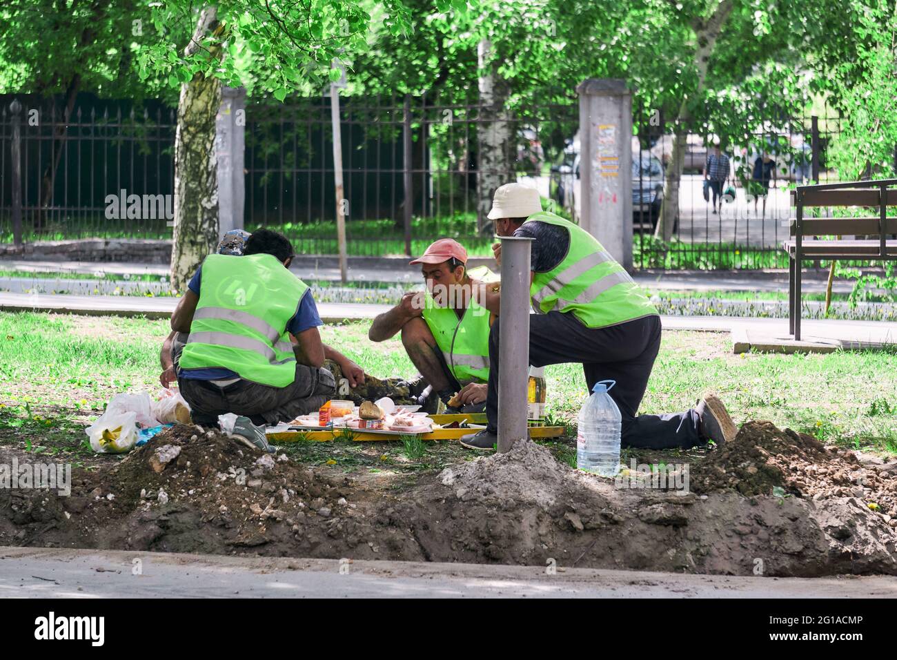 Perm, Russland - 18. Mai 2021: Brigade von Straßengastarbeitern essen während einer Pause auf der Straße zu Mittag Stockfoto