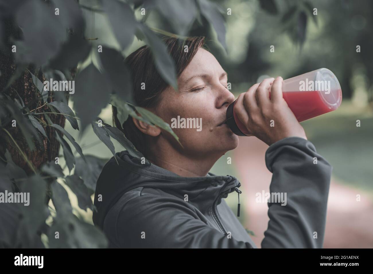 Joggerin trinkt erfrischenden Erdbeersaft im Park, gesunden Lebensstil und Freizeitaktivitäten in den 40er Jahren Stockfoto