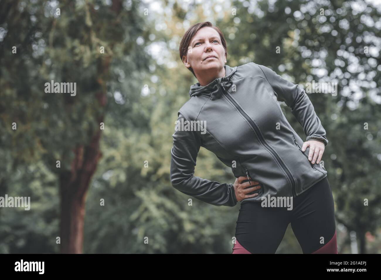 Porträt einer erwachsenen Joggerin, die sich in den 40er Jahren im Park dehnt und sich aufwärmt, um auf der Strecke zu laufen, gesund zu leben und sich zu sportlich zu betätigen Stockfoto
