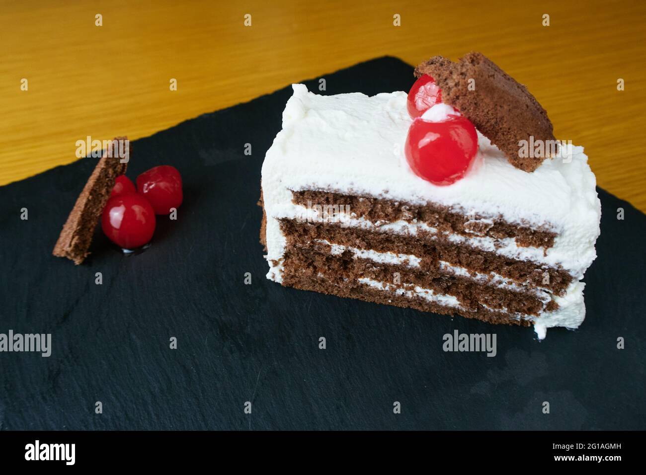 Schwarze Waldscheibe, verziert mit Kirschen und kleinen Kuchenstücken auf einem schwarzen Schieferbrett Stockfoto
