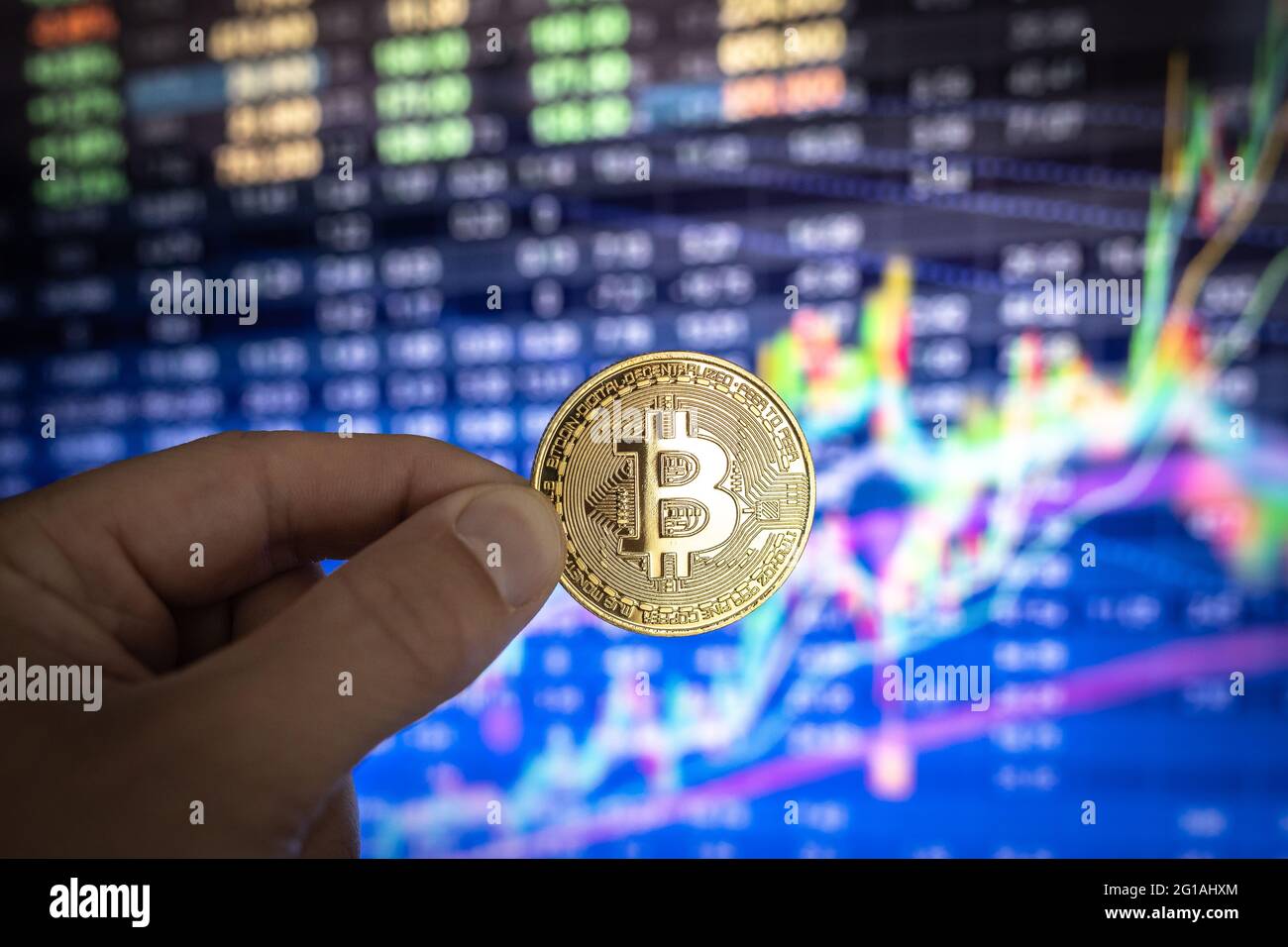 Bitcoin physische Münze vor bunten Diagrammen und Grafiken. Stockfoto