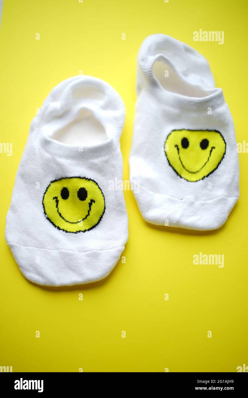 Zwei weiße Socken mit einem Smiley-Gesicht auf einem leuchtend gelben Tisch. Stockfoto