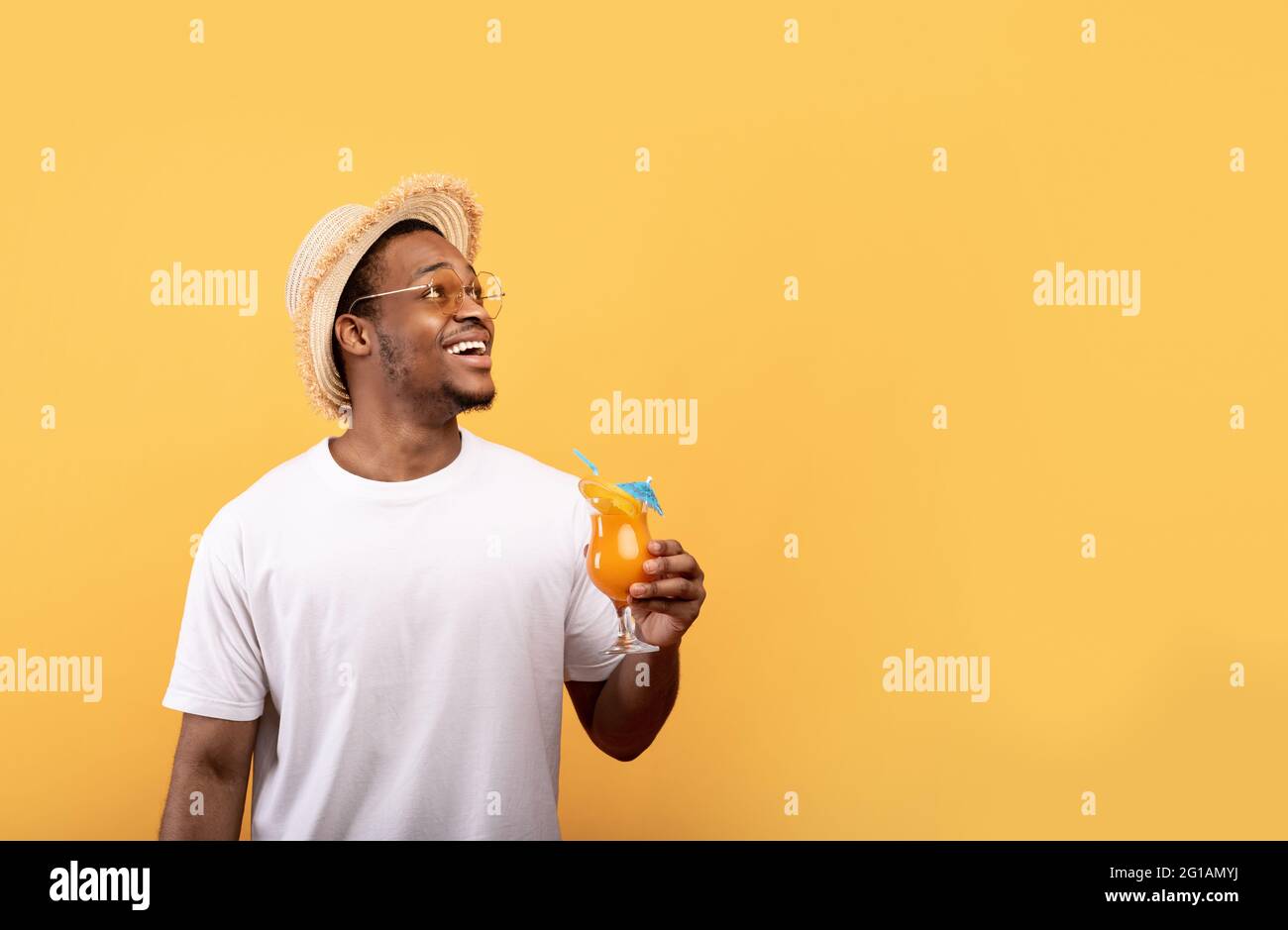 Super Sommerangebot. Fröhlicher afroamerikanischer Mann mit einem köstlichen tropischen Cocktail, der auf leeren Raum blickt Stockfoto