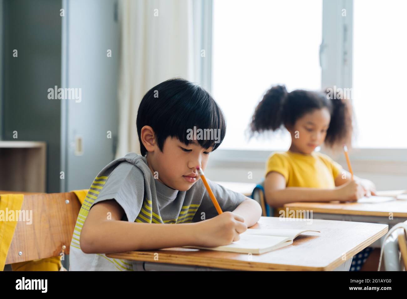 Schulkinder, die in der Schule am Schreibtisch sitzen und mit Bleistift ein Notizbuch schreiben, lernen, lernen und lernen. Schülerinnen und Schüler im Klassenzimmer. Junge und Mädchen im Grundalter Stockfoto