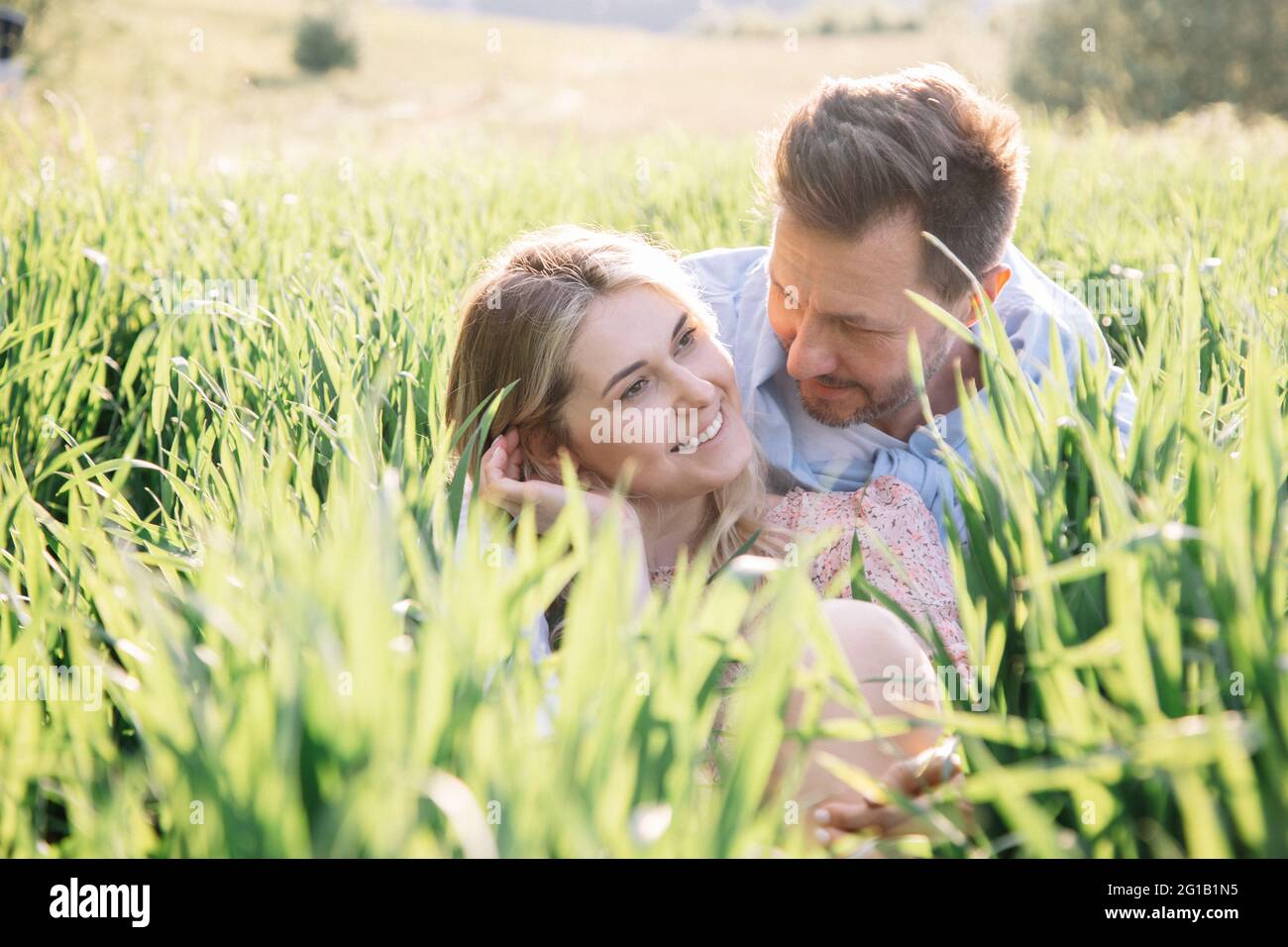 Flirten und lächeln der jungen schönen Blondine auf dem ersten Date mit dem Mann. Foto eines Paares, das im grünen Gras sitzt Stockfoto