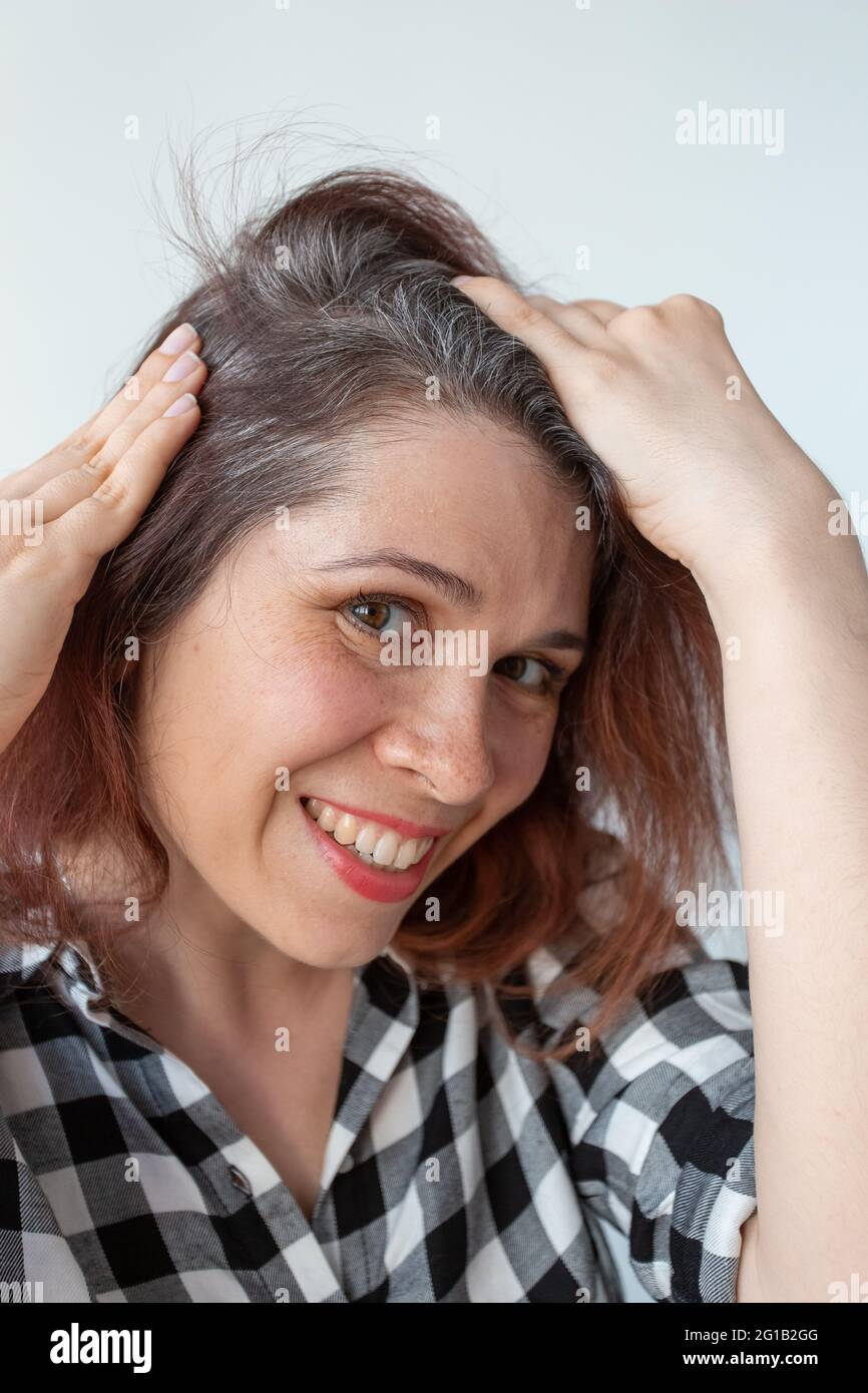 Die junge Frau zeigt ihre grauen Haarwurzeln. Konzept für die frühzeitige Alterung. Stockfoto