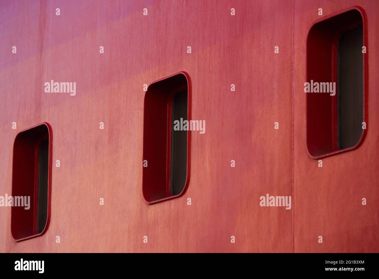 Drei rechteckige Bullaugen auf EINEM roten Schiffsrull Stockfoto