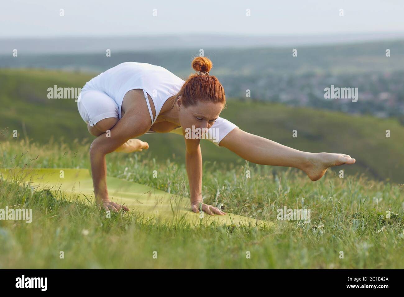 Konzentrierte Frau, die ihren Körper trainiert und die Armbalance in Posen übt Frische grüne Wiese Stockfoto