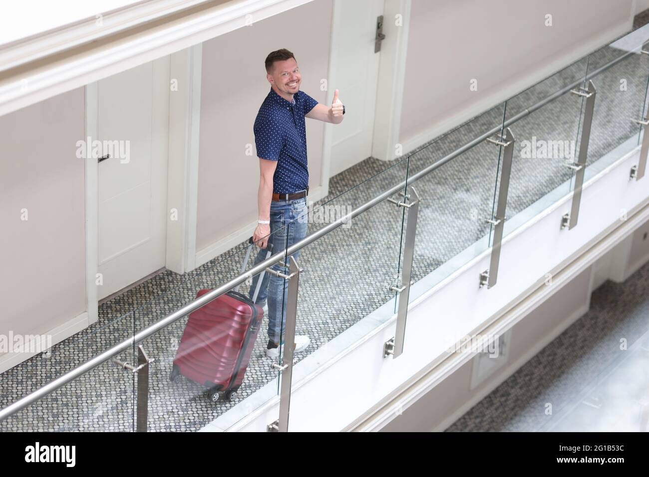 Ein junger lächelnder Mann steht im Hotelkorridor und zeigt die Daumen nach oben Stockfoto