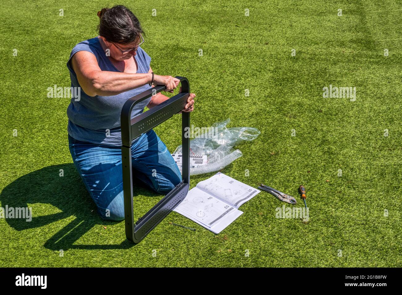 Frau, die draußen einen selbstzusammenbauenden Grill mit Werkzeugen und Anweisungen baut. Stockfoto