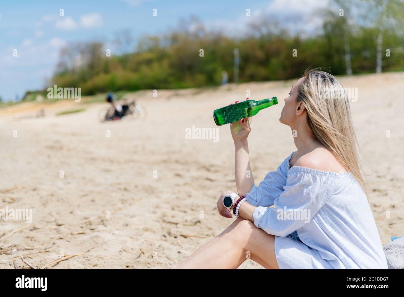 Die attraktive Frau hält im Sommer eine Flasche kaltes Bier am Strand in der Nähe des Sees. Stockfoto