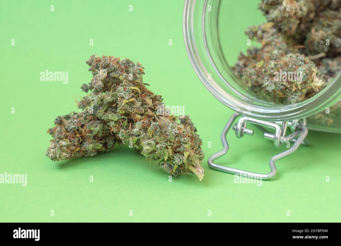 Trockene Knospen von Marihuana in einem Glasgefäß in Nahaufnahme auf grünem Hintergrund. Stockfoto