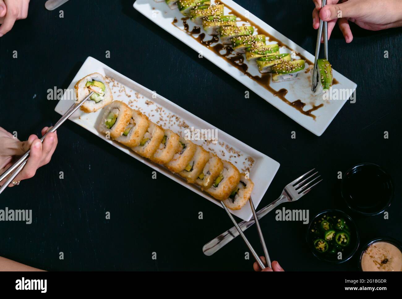Anonyme Freunde aus einem hohen Blickwinkel mit wiederverwendbaren Essstäbchen, die köstliche Sushi-Brötchen mit Sojasauce und Jalapeno-Pfeffer essen Stockfoto