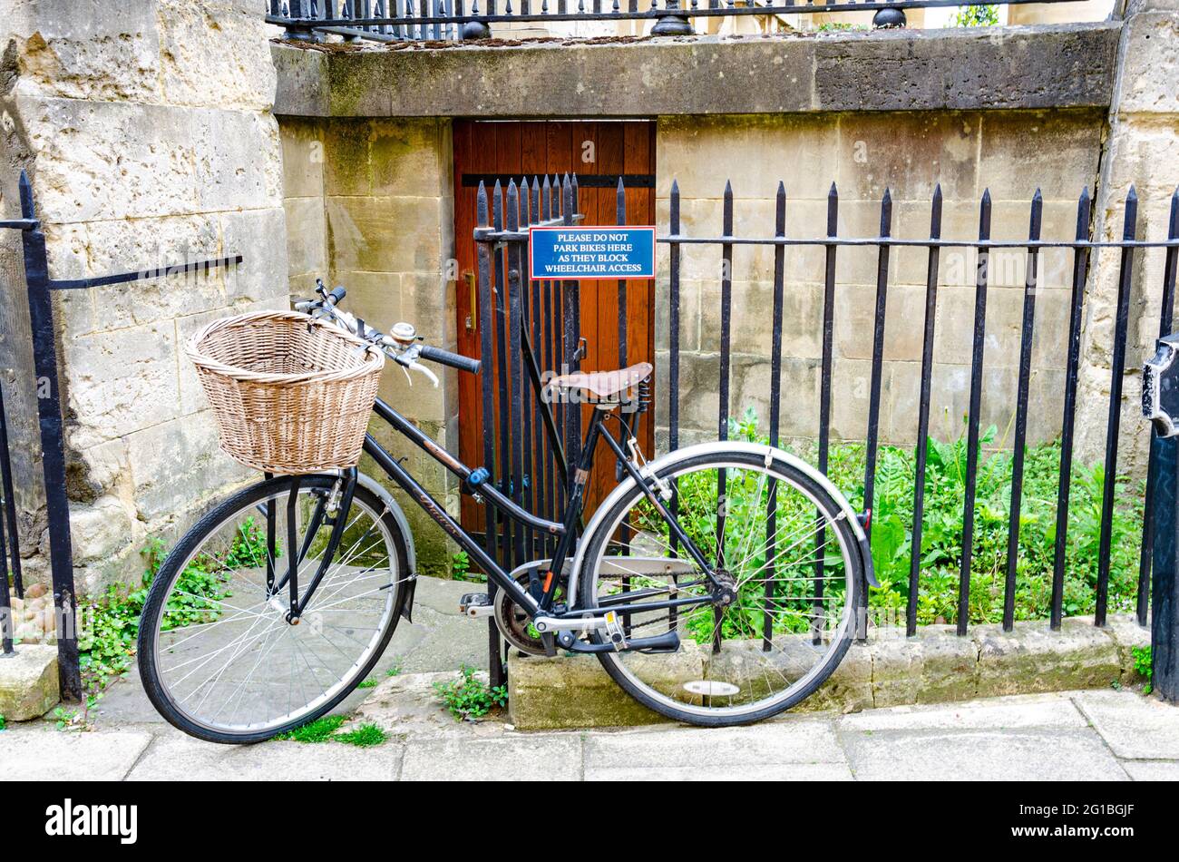 Ein Fahrrad lehnte sich im Widerspruch zu dem Schild, das darauf hinwies, dass keine Fahrräder auf dem Geländer geparkt werden sollten, gegen ein schwarzes Geländer. Stockfoto