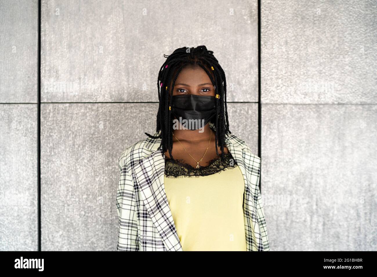 Enttäuschte afroamerikanische Frau in Maske, die gegen eine graue Wand stand und mit Traurigkeit auf die Kamera schaute Stockfoto