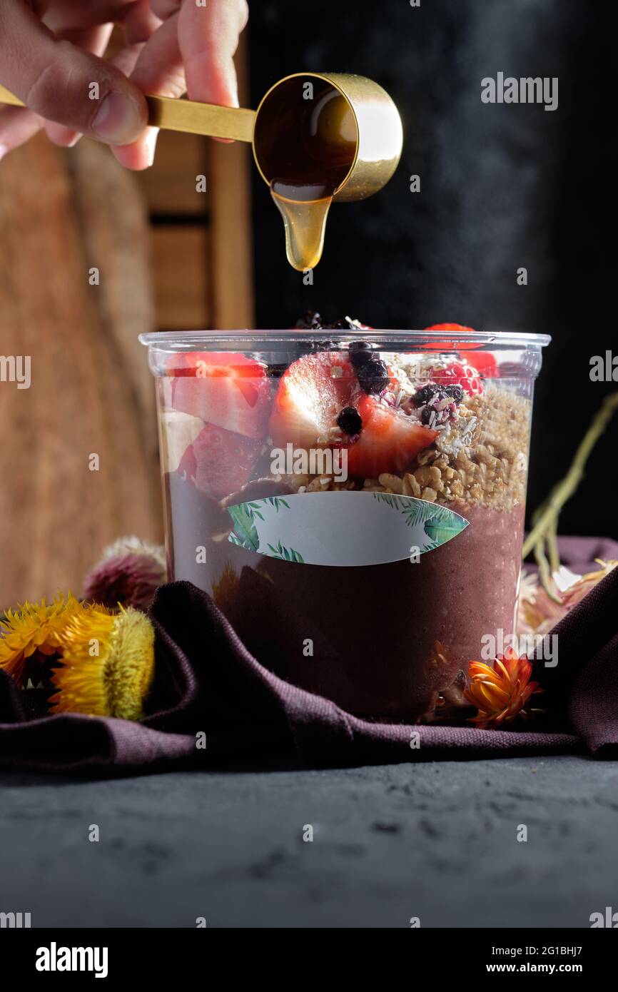 Crop anonyme Person gießt Honig in eine Schüssel appetitlich kalten Smoothie mit Müsli und frischen Beeren gekrönt Stockfoto