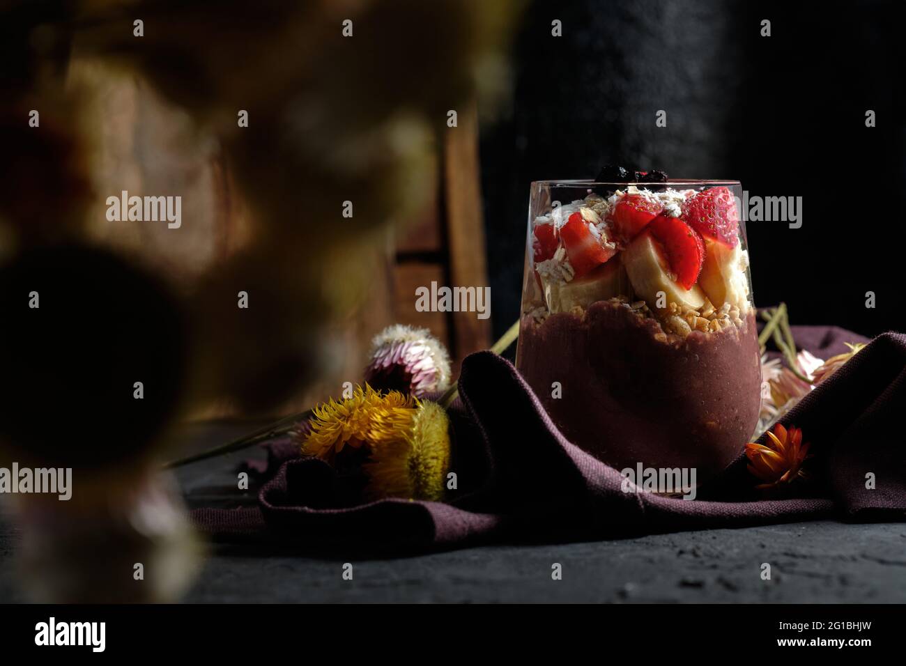 Appetitliche Smoothie-Schale mit Granola-Erdbeeren und Heidelbeeren auf dem Tisch in der Nähe verschiedener Wildblumen Stockfoto