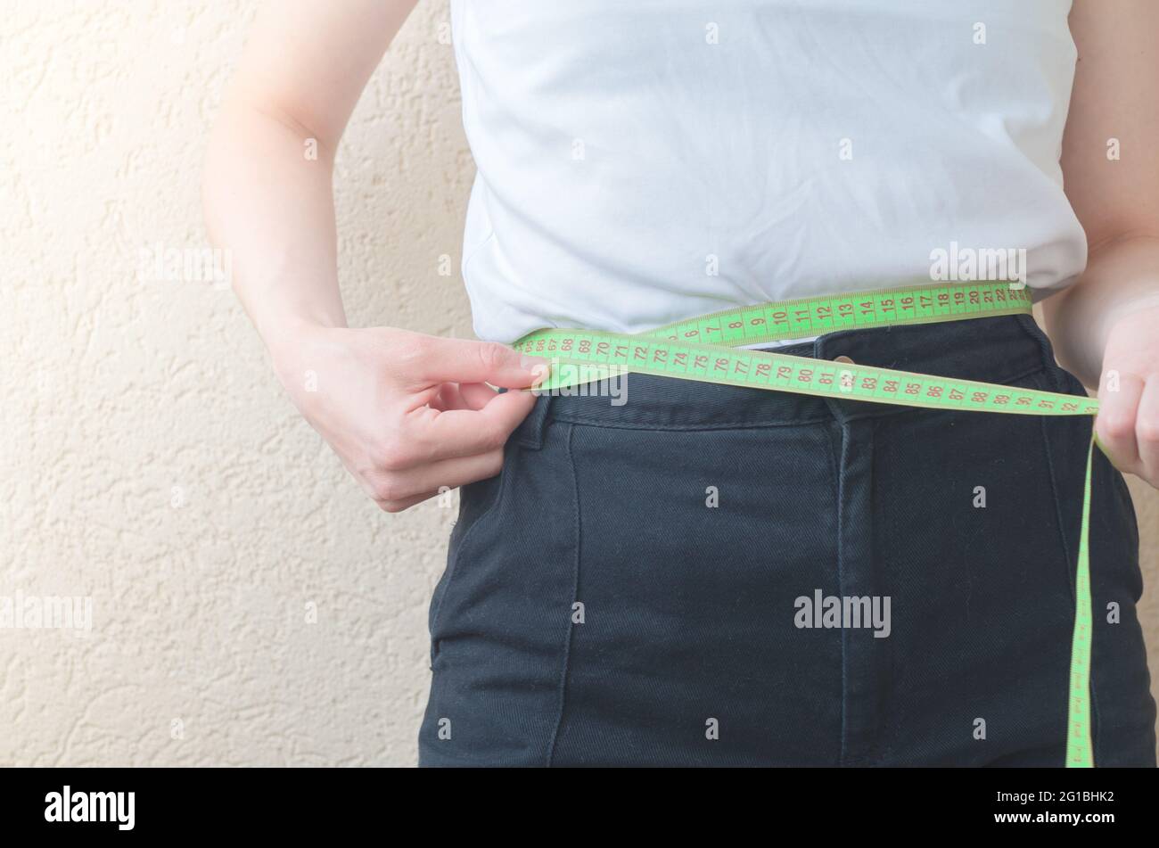 Nahaufnahme EINE Frau in Freizeitkleidung misst ihre Taille mit EINEM Maßband Stockfoto