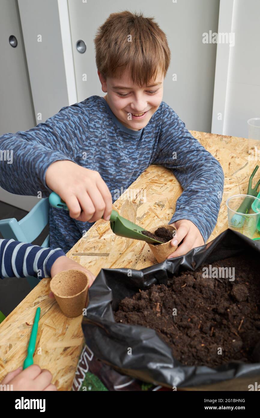 Glückliches Kind mit Gartenschaufel, der den Öko-Becher mit Erde am Tisch füllt Stockfoto