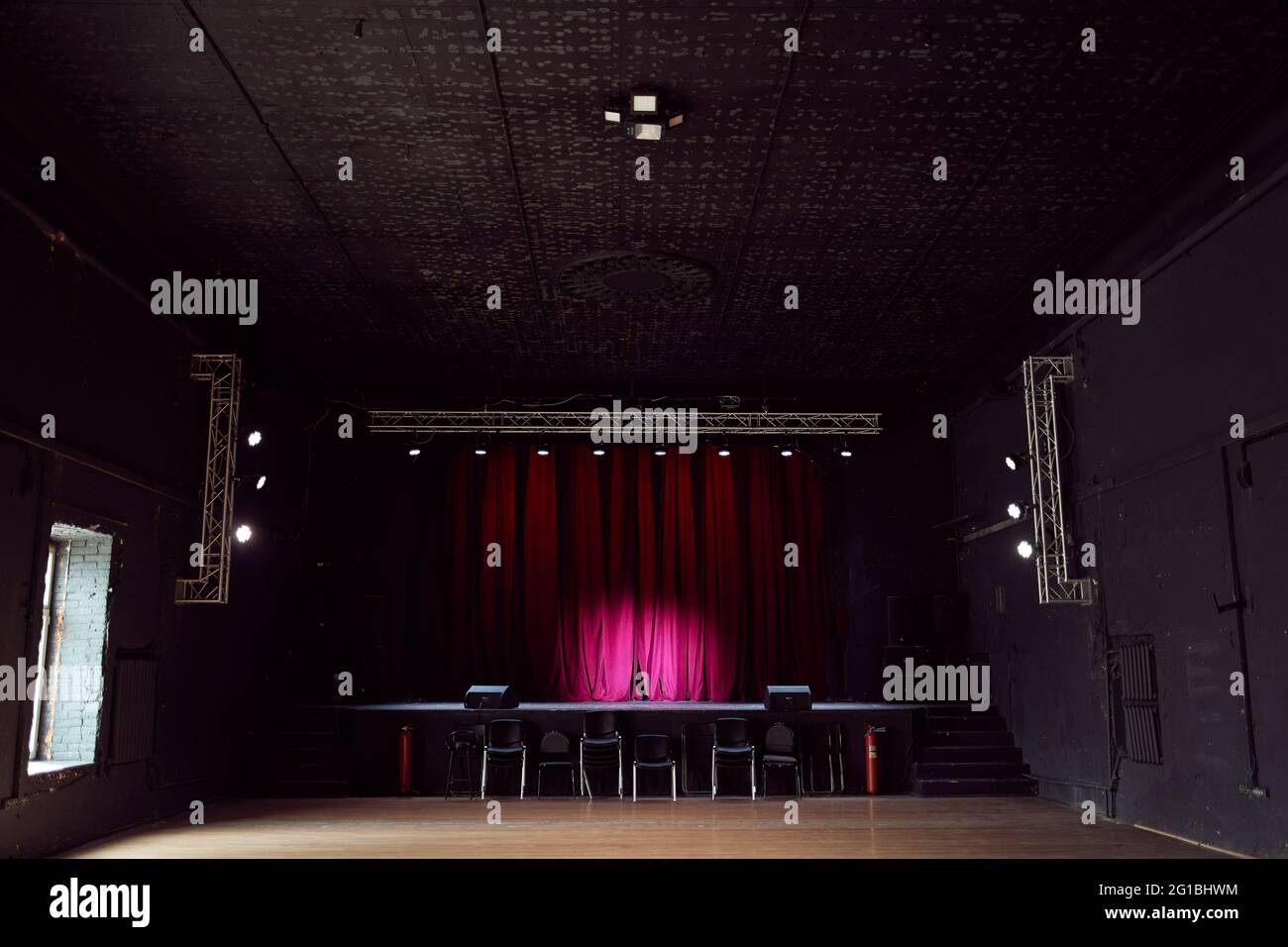 Innenraum eines leeren Konzertsaals ohne Stühle und einer kleinen Bühne mit violetten Vorhängen Stockfoto