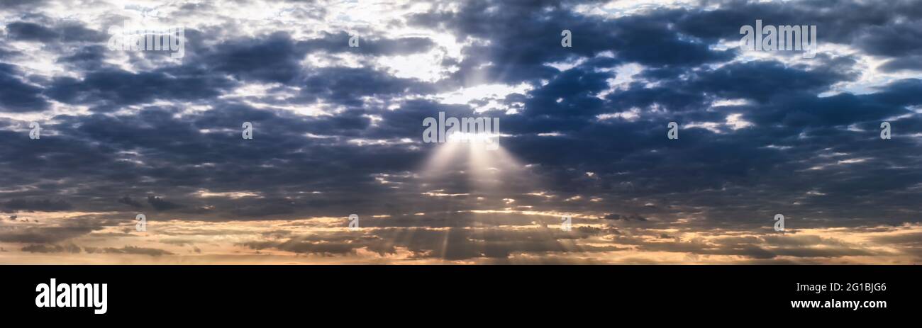 Panorama von orange und dunkelblau dramatischen Himmel mit Wolken bei Sonnenuntergang, Sommerabend. Die Sonnenstrahlen brechen durch die dunklen Wolken. Unschärfe in Bewegung. Stockfoto