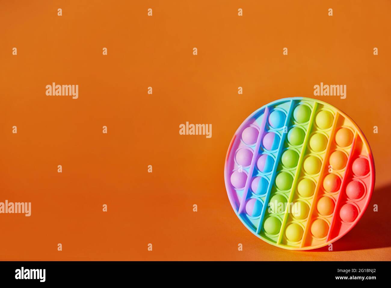 Pop it Spielzeug auf orangefarbenem Hintergrund mit Kopierraum. Beliebte mehrfarbige Silikon Anti-Stress-Spielzeug. Stockfoto