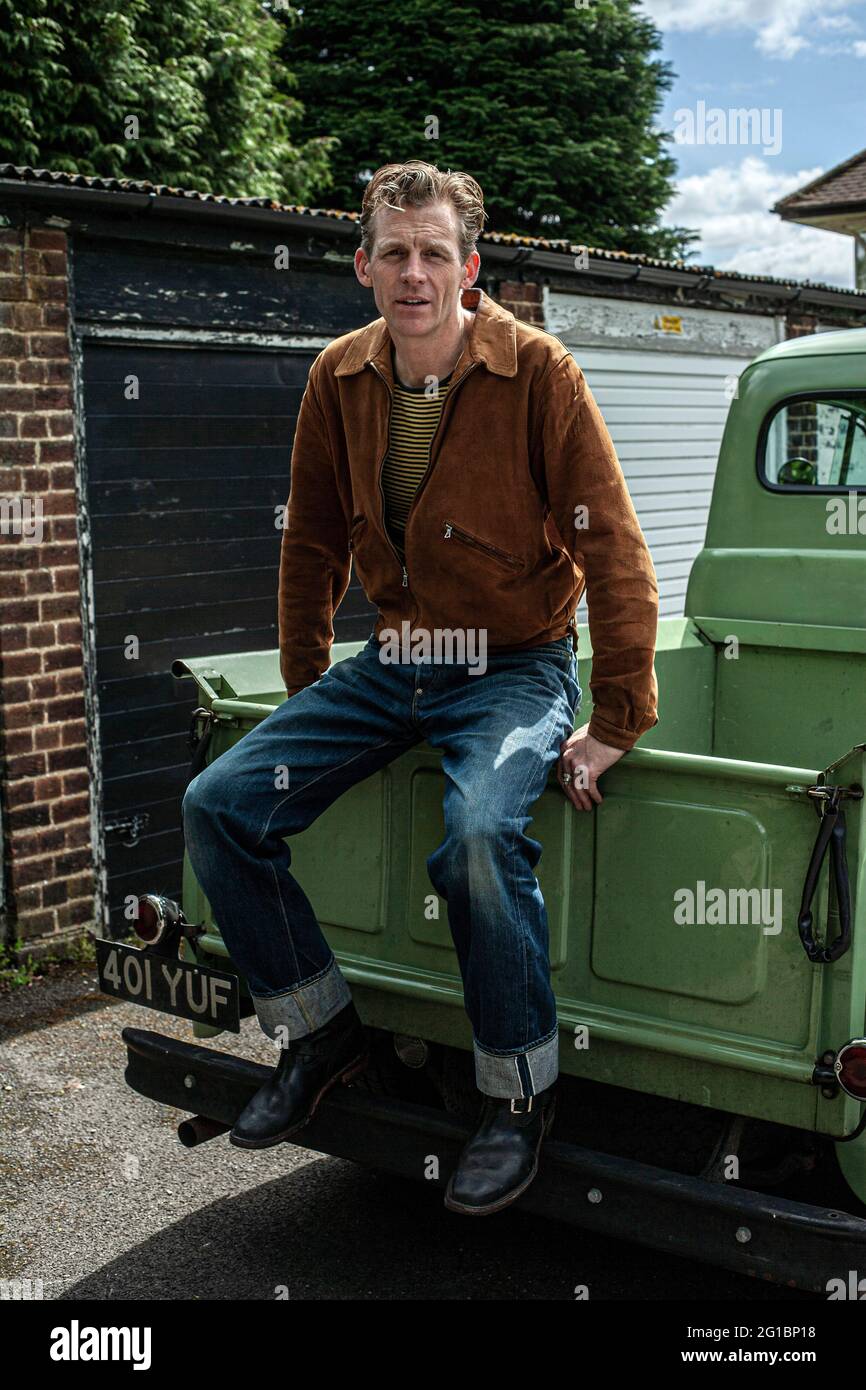 Mann in Jeans sitzt auf seinem Ford F 1 Pick-up-Truck. Mann, der auf dem Rücken eines alten Ford-Pick-up-Trucks sitzt. Stockfoto