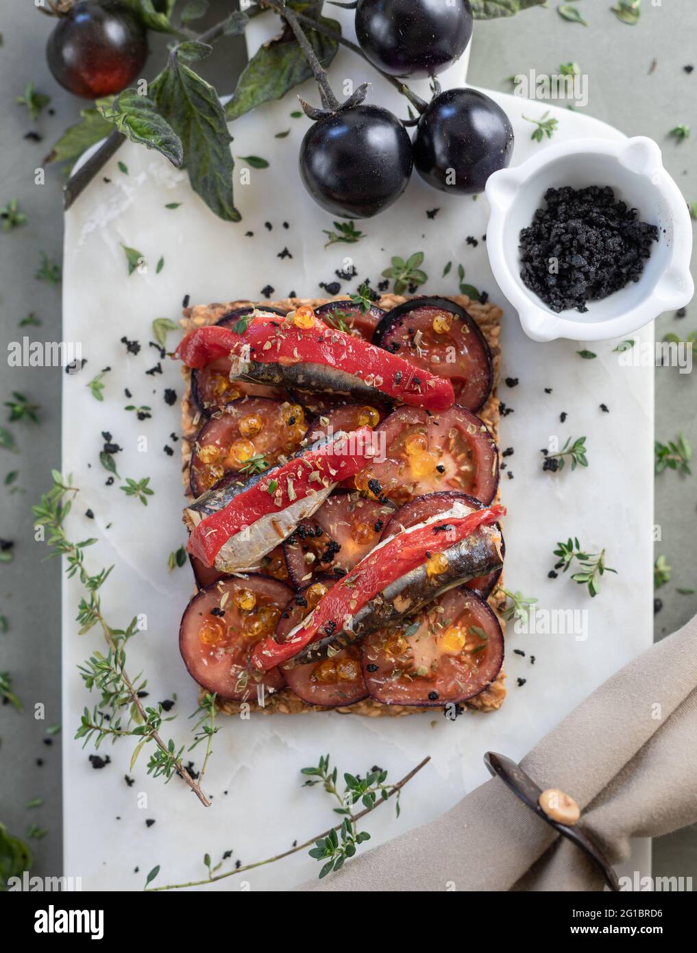 Sardine in Olivenöl, Toast mit schwarzen Tomaten und Kräutern auf Marmorplatte Stockfoto