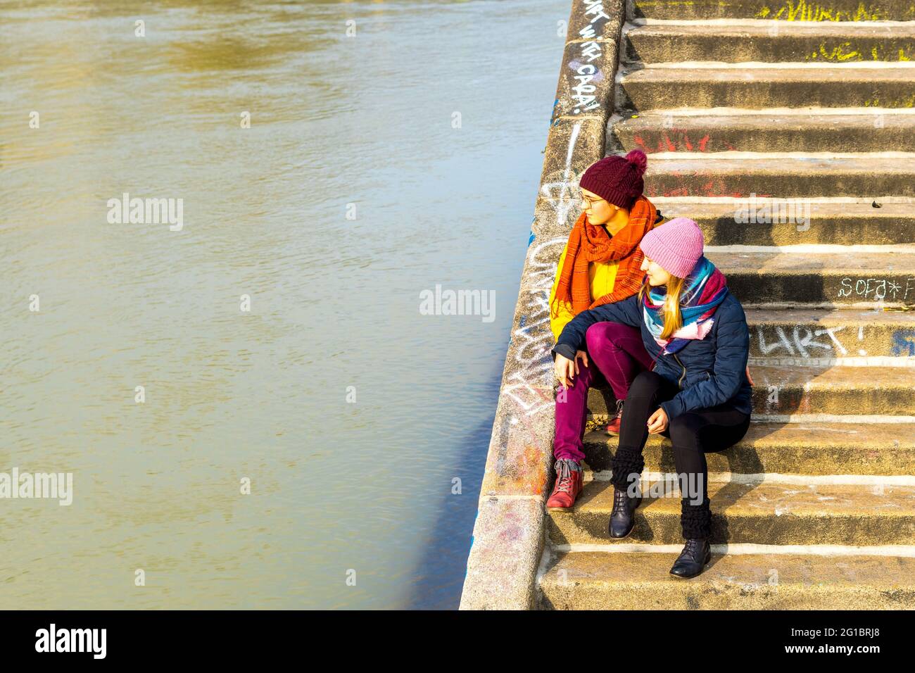 Die beiden Freundinnen sitzen auf der Treppe am Fluss, Österreich Stockfoto