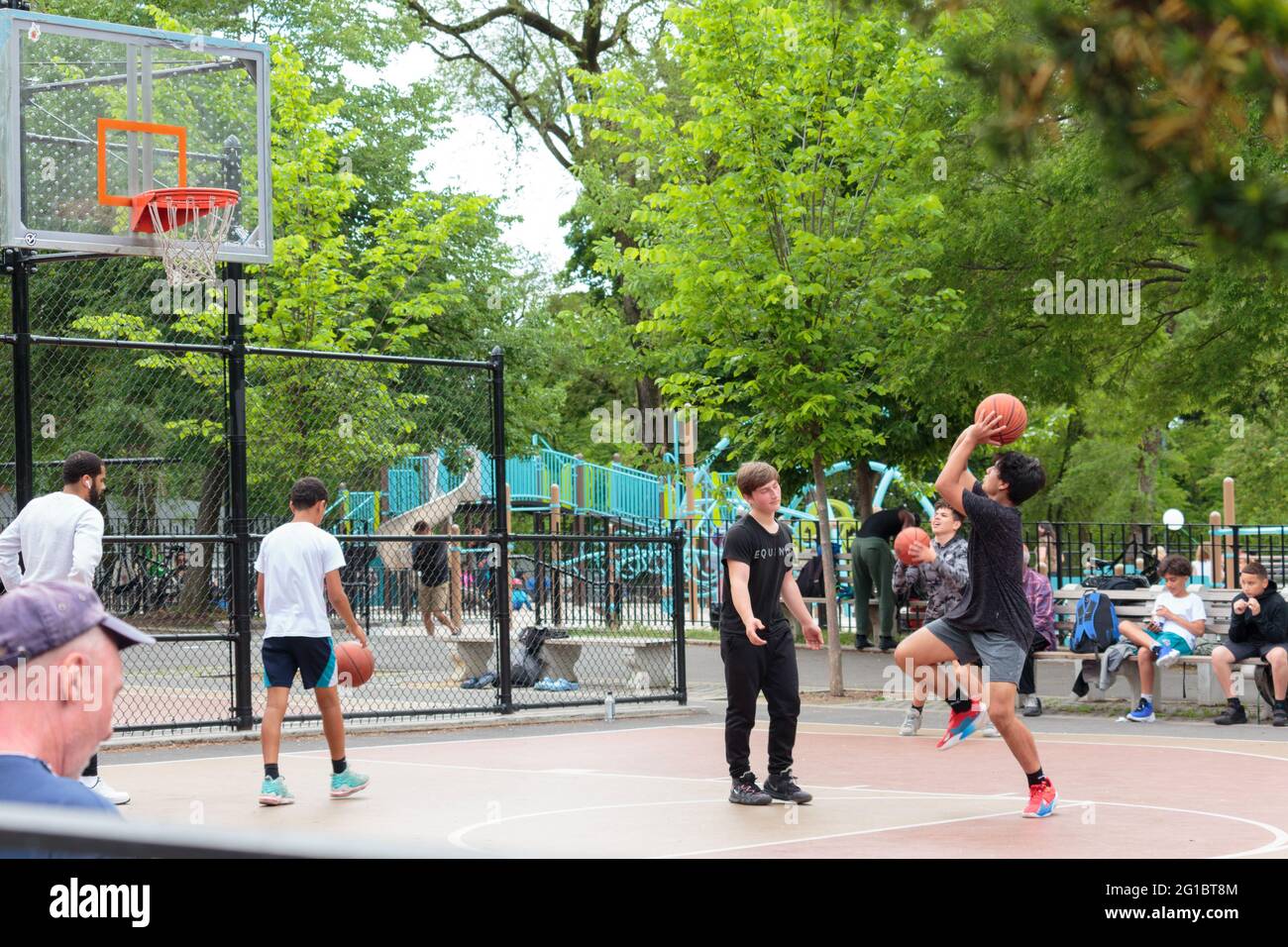 Jugendbasketballspiel in einem New yorker Stadtpark schieß ein Junge, der Ball liegt noch in seinen Händen, während ein anderer Wache hält Stockfoto