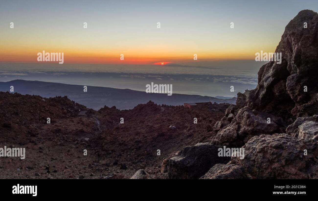 Orangerote Sonne, die über den flauschigen Wolken vom Gipfel des Pico del Teide mit Seilbahn aufgeht Station, Teneriffa, Spanien Stockfoto