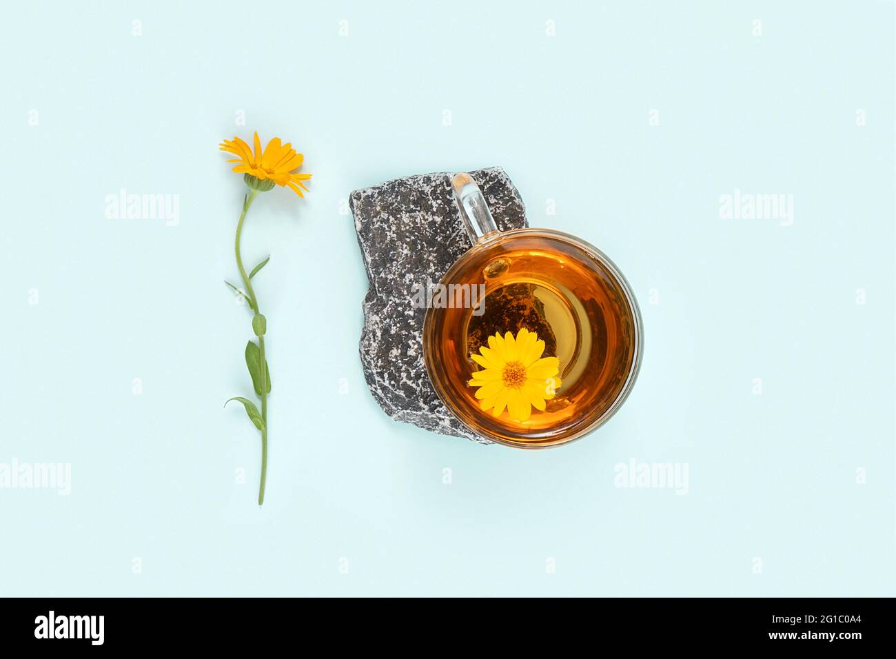 Tasse Kräutertee auf Stein und Ringelblume auf blauem Hintergrund. Beruhigendes Getränkekonzept. Stockfoto
