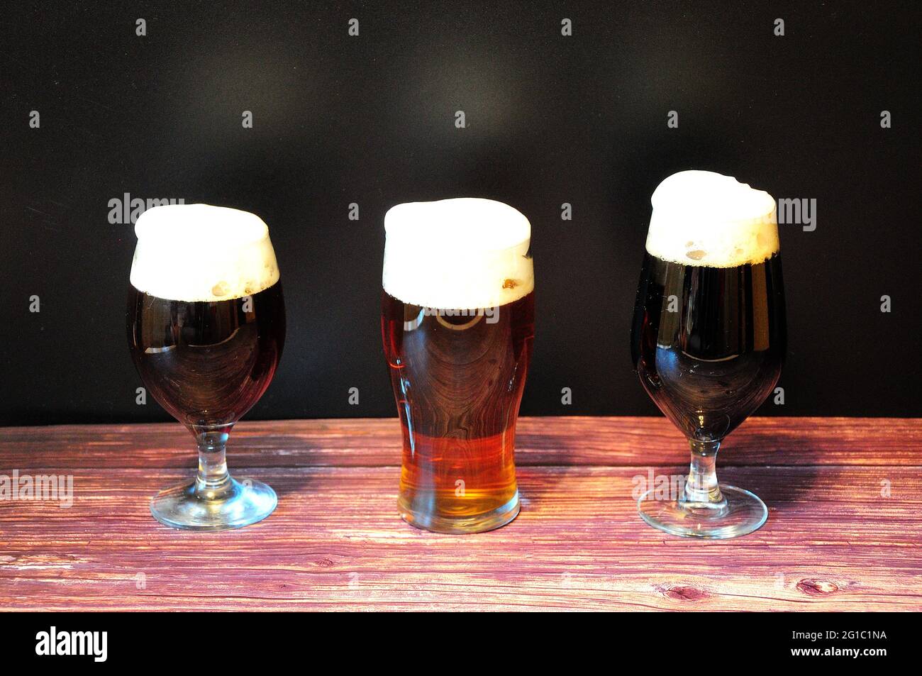 Drei Gläser mit verschiedenen dunklen Biersorten stehen auf einem Holztisch. Nahaufnahme. Stockfoto