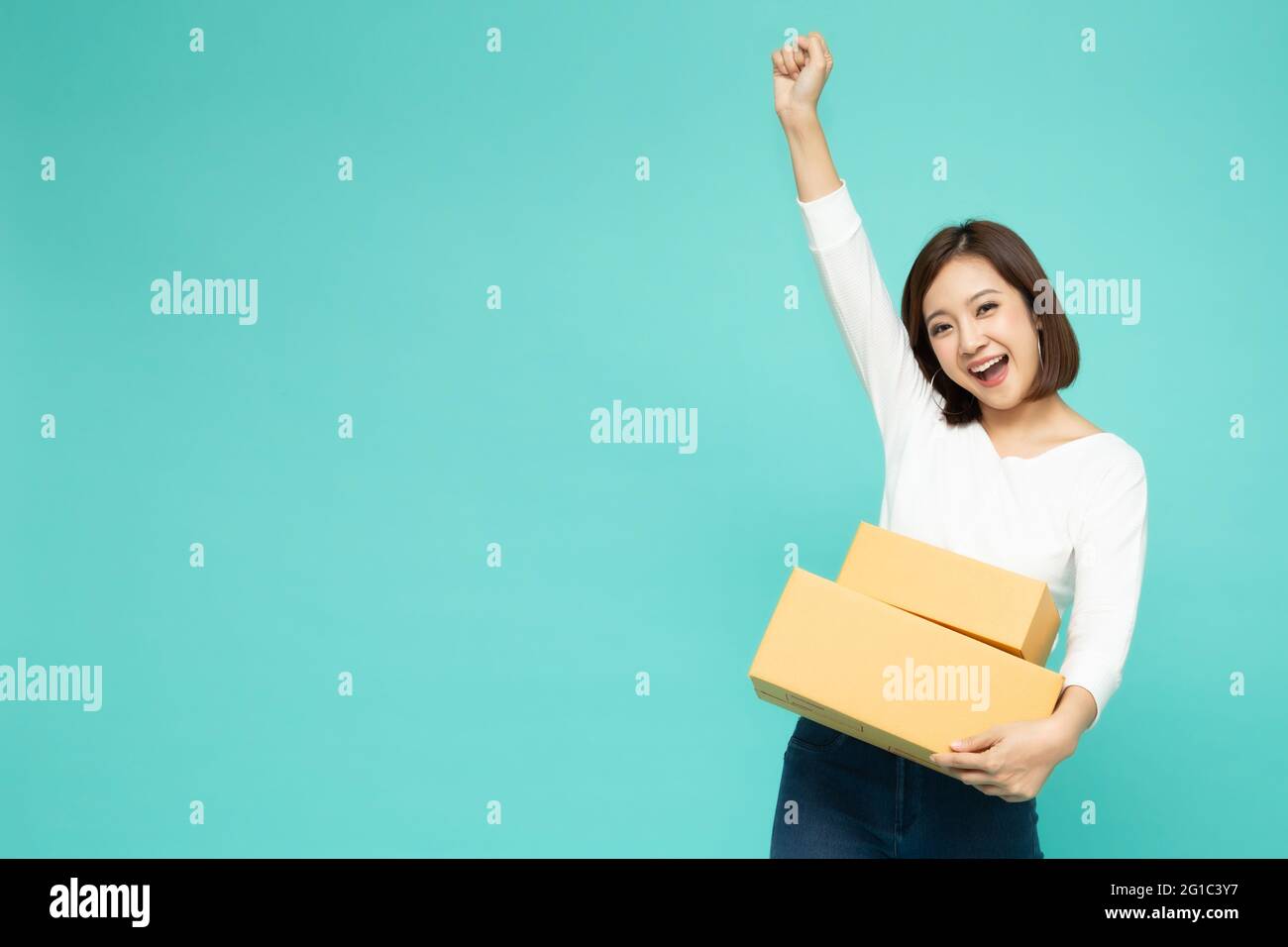 Glückliche asiatische Frau hält Paket Paketkasten und feiert Erfolg mit Händen in der Luft isoliert auf hellgrünem Hintergrund, Lieferung Kurier und sh Stockfoto