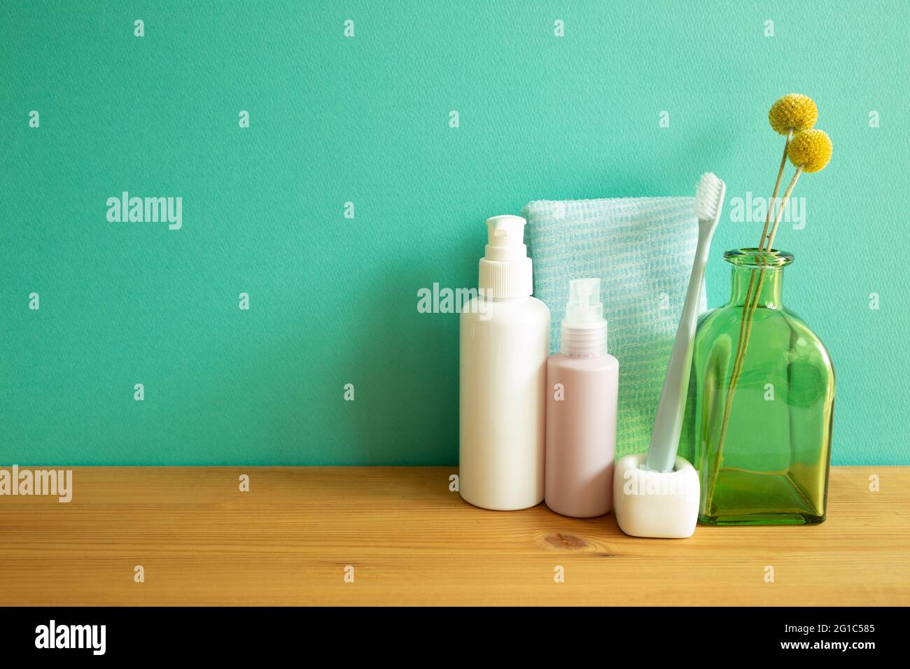 Badezimmer Flaschen, Duschtuch, Zahnbürste, Vase mit Pflanzen auf Holztisch. Minze Wand Hintergrund. Hautpflege- und Spa-Konzept Stockfoto