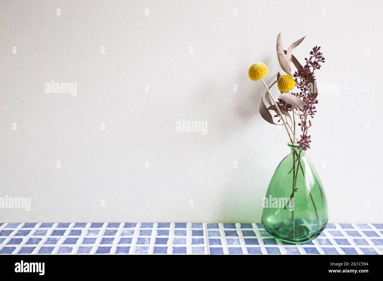 Vase mit trockenen Blumen auf blauem Keramik-Mosaik-Fliesentisch. Weißer Wandhintergrund. Inneneinrichtung Stockfoto