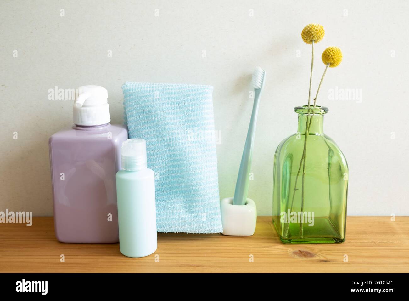Badflaschen, Duschtuch, Zahnbürste, Vase mit Pflanzen auf Holztisch. Weißer Wandhintergrund. Hautpflege- und Spa-Konzept Stockfoto