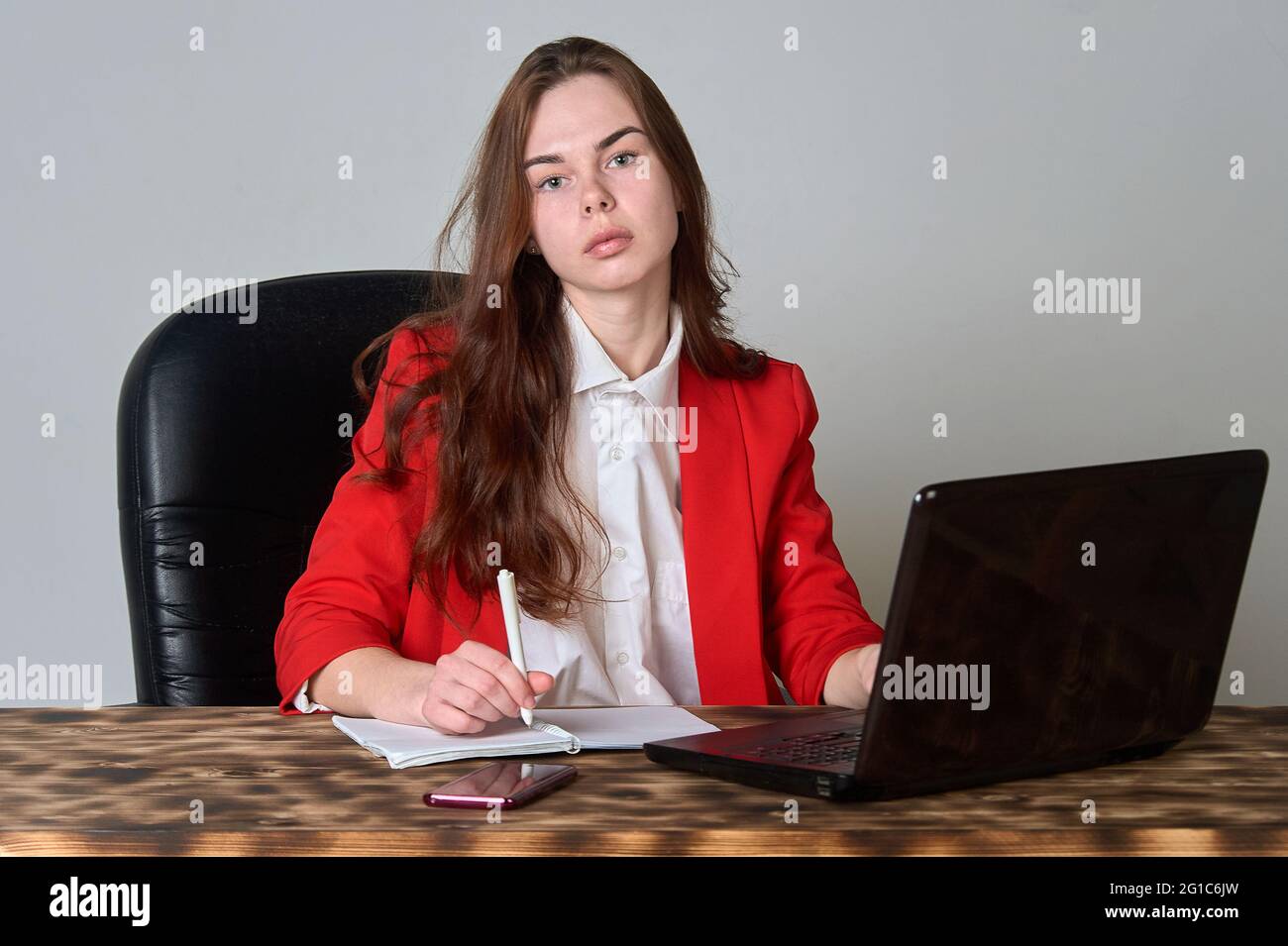 Eine Frau, die an einem Schreibtisch sitzt und mit einem Laptop arbeitet Und Notizblock Stockfoto