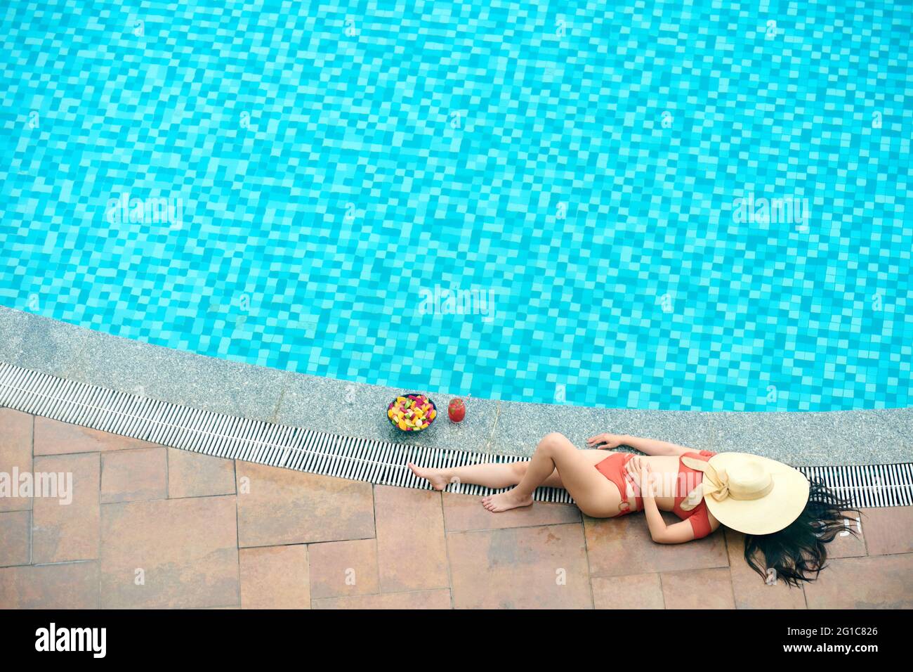 Schöne junge Frau im Bikini, die Gesicht mit Strohhut bedeckt, wenn sie am Pool sonnenbaden Stockfoto