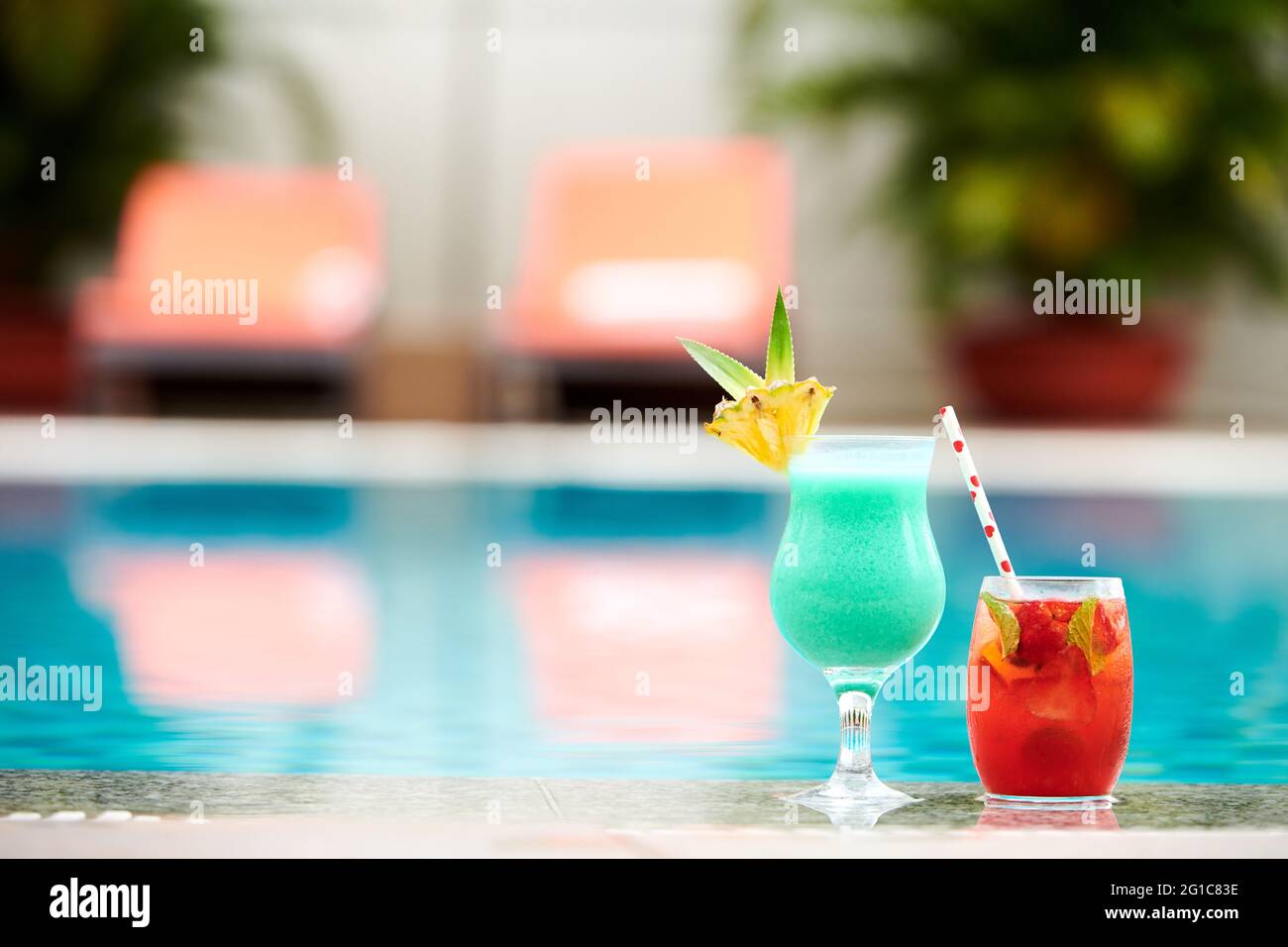 Dekorierte Gläser mit süßen, köstlichen Türkis- und roten Fruchtcocktails am Rand des Swimmingpools Stockfoto