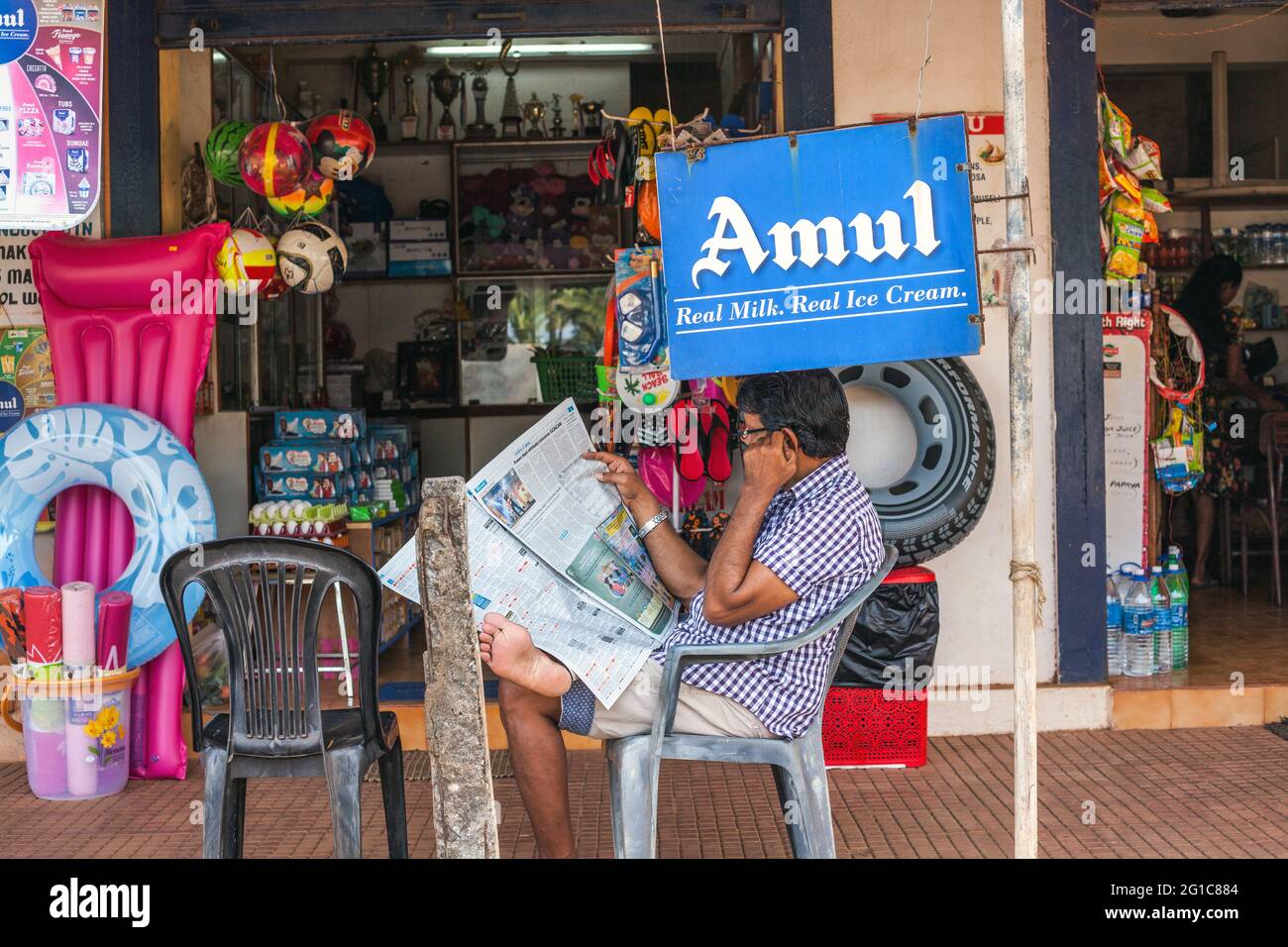 Der indische Gentleman liest vor dem 24-Stunden-Geschäft, in dem Strandzubehör verkauft wird, Agonda, Goa, Indien Stockfoto