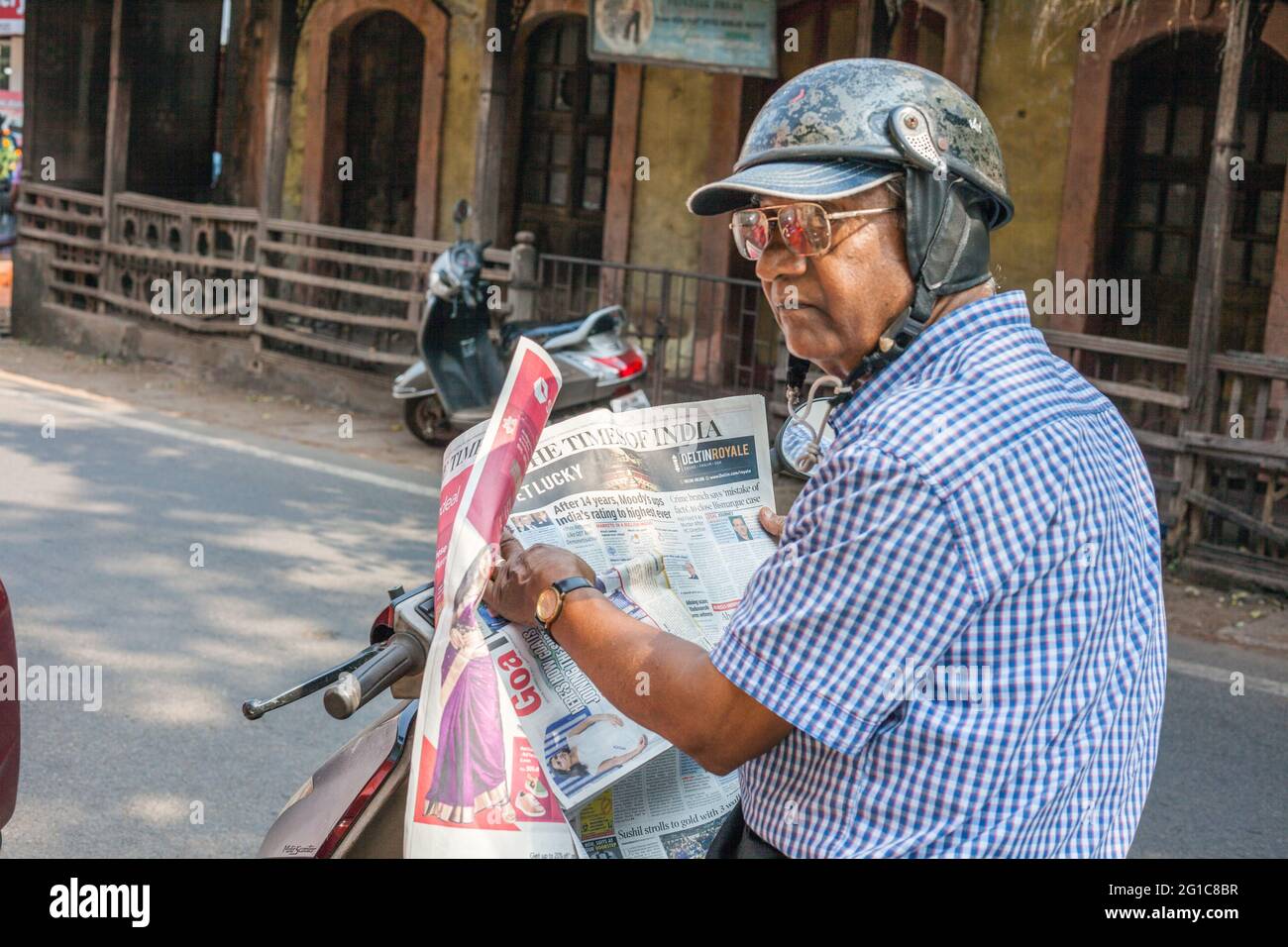 Älterer indischer Herr saß auf dem Roller und las die Zeitung „The Times of India“, Margao, Goa, Indien Stockfoto