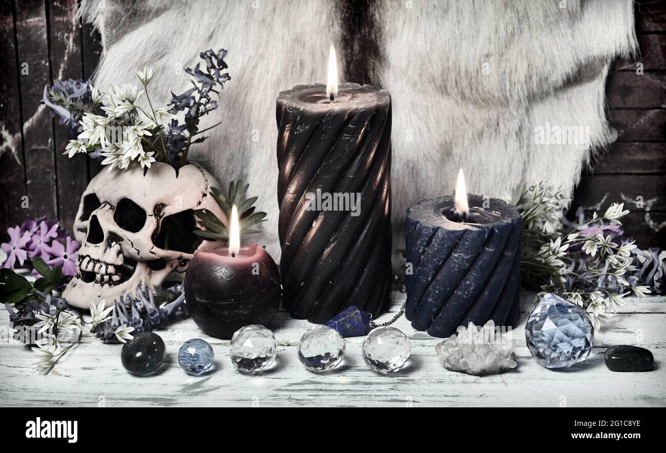 Grunge Stillleben mit Kristallsteinen, brennenden Kerzen und Totenkopf mit Blumen auf Hexenaltar Tisch. Esoterischer, gotischer und okkulter Hintergrund, Halloween Stockfoto